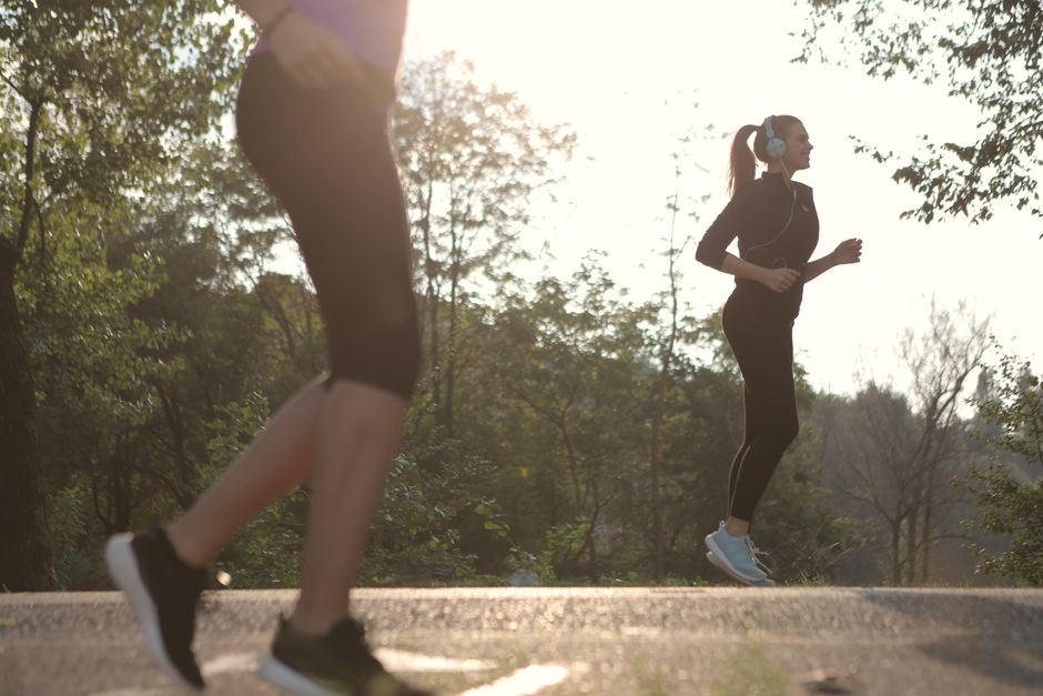 Two women jogging in a sunny park setting, enjoying a healthy morning exercise.